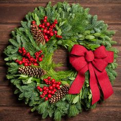 a christmas wreath with pine cones, holly and red berries on a wooden table top