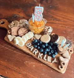 a wooden tray topped with cookies and crackers next to a cup filled with blueberries