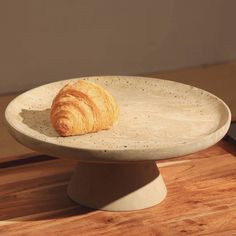 a croissant sitting on top of a white plate next to a brown wall