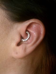 a woman's ear is shown with three small white stones in the shape of a crescent