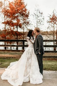 a bride and groom standing next to each other in front of some trees with orange leaves