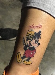 a person with a mickey mouse tattoo on their left leg and the word nud written in red ink