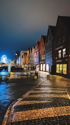 a city street at night with colorful buildings and ferris wheel in the background