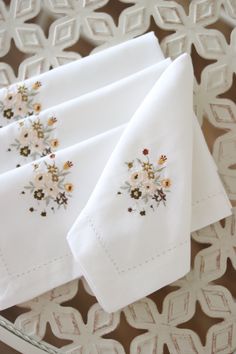 three white napkins with embroidered flowers on them