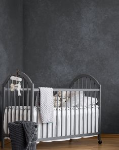 a baby crib in a room with grey walls and wood flooring, along with a teddy bear on the bed