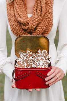 a woman holding a red box with cookies in it and a scarf around her neck