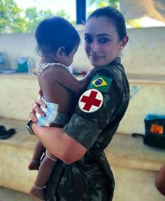 a woman holding a child in her arms while wearing an army uniform with the flag of brazil on it