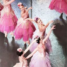 four ballerinas in pink tutu skirts and flowered headbands are dancing