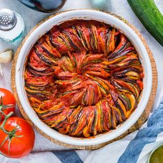 a vegetable dish in a white bowl with tomatoes and cucumbers around it