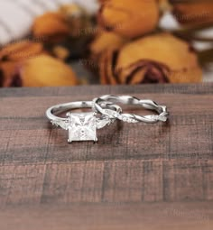 two wedding rings on top of a wooden table with flowers in the backgroud