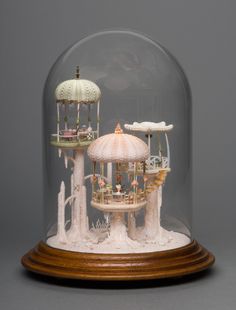 a carousel under a glass dome on a wooden base with other items underneath it, all in white and gold