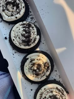 four cookies with white frosting and black sprinkles on them sitting in a box