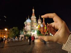 a hand is holding up a miniature model of a city at night with people walking around