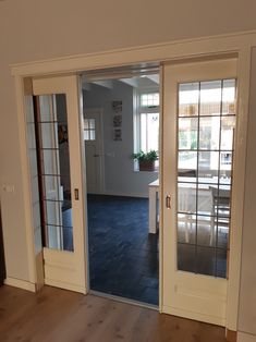 an open door leading to a kitchen and dining room area with hardwood floors, white walls and glass doors