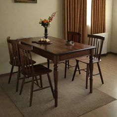 a dining room table with four chairs and a vase on top of it in front of a window