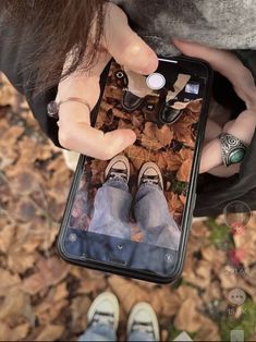 a person holding an iphone in their hands with leaves on the ground and shoes around them