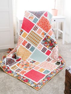 a patchwork quilt sitting on top of a bed next to a wooden dresser and window