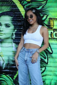 a woman standing in front of a wall wearing jeans and a crop top with her hands on her hips