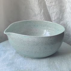 a white bowl sitting on top of a blue cloth covered table next to a wall