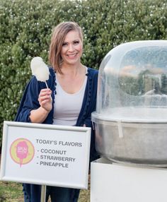 a woman holding a lollipop standing next to a large ice cream dispenser