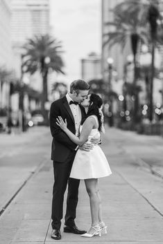 black and white photograph of a couple kissing on the sidewalk in front of palm trees