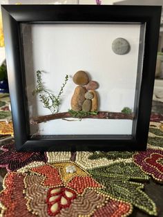 two rocks sitting on top of a tree branch in a framed black frame next to a plant