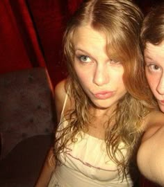 two young women posing for the camera in front of a red curtain, one with her arm around the other's shoulder