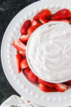 a white plate topped with strawberries on top of a black countertop next to a bowl of whipped cream