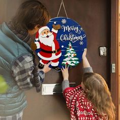 a woman and child are hanging a merry christmas sign