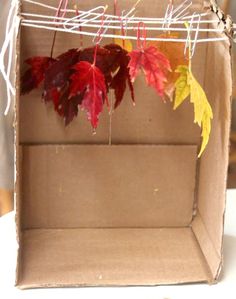 an open cardboard box with autumn leaves hanging from the top and string attached to it