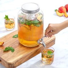 a person pours tea into a glass pitcher on a cutting board with peaches and mint