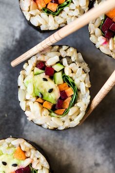 three sushi rolls with vegetables and rice on top, next to chopsticks