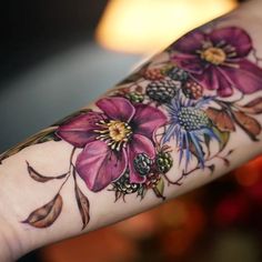 a woman's arm with purple flowers on it and leaves around the wrist area