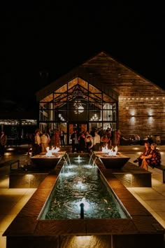 people are gathered around an outdoor fire pit at night with lights on the roof and water running through it