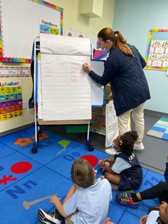 a group of children sitting on the floor in front of a white board