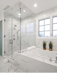 a white bathroom with marble walls and flooring, along with a walk in shower