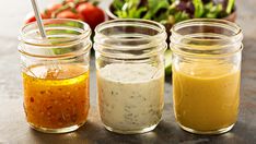 three jars filled with different colored sauces on top of a table next to a salad