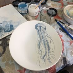 a bowl with a jellyfish drawn on it next to some paint and watercolors