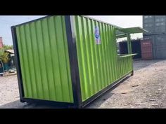 a green shipping container sitting on top of a dirt field next to a metal structure