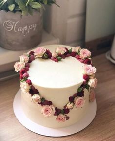 a white cake with pink and red flowers on it sitting on a table next to a potted plant