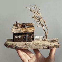 a hand holding a piece of wood with a house on it and a tree branch