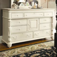 a white dresser with a mirror on top of it next to a lamp and window