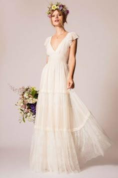 a woman in a long white dress with flowers on her head is holding a bouquet