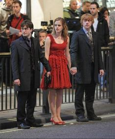 three people standing on the street in front of a crowd, one wearing a red dress