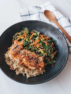 a black bowl filled with rice, meat and veggies on top of a white table