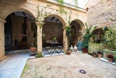 an outdoor patio with potted plants and tables in the center, surrounded by brick arches