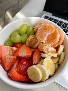 a white bowl filled with fruit next to a laptop