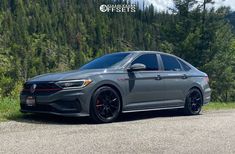 a gray car parked on the side of a road next to some trees and bushes