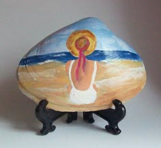 a painted rock with an image of a woman in white dress on the beach and black legs