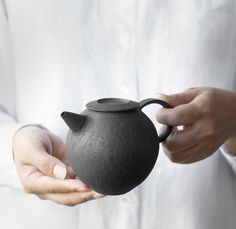 a person holding a black teapot in their hands